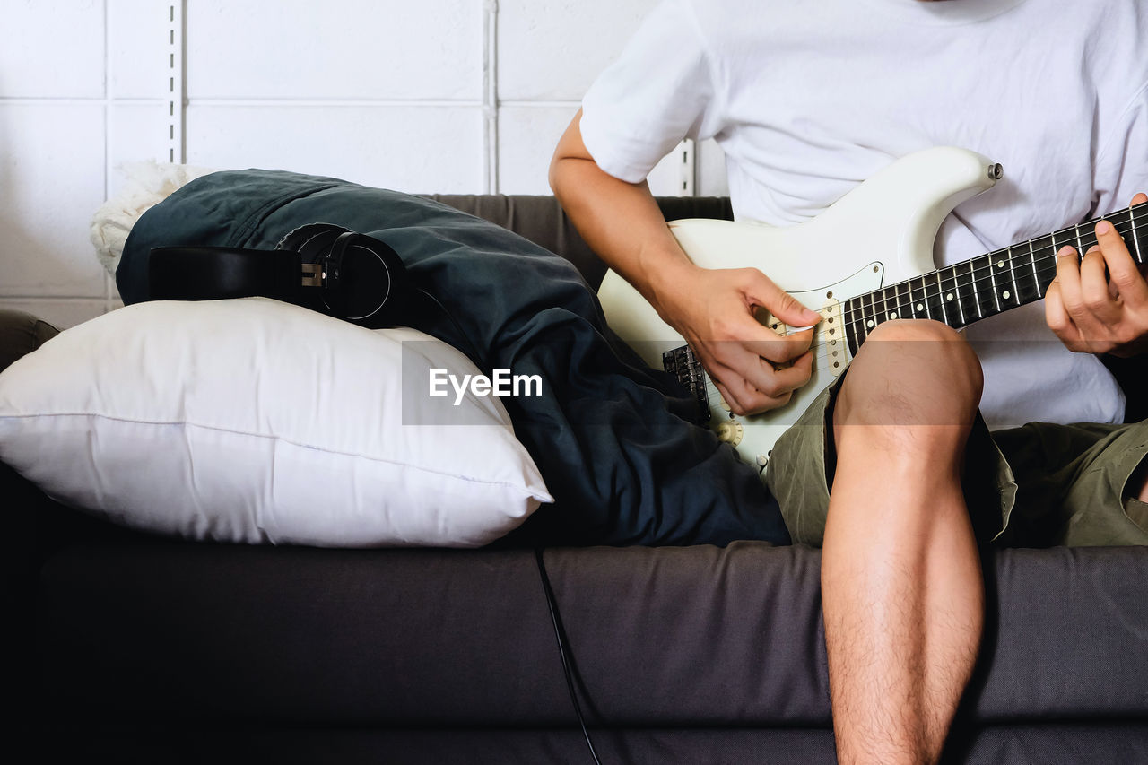 Man playing electrical guitar on sofa at home