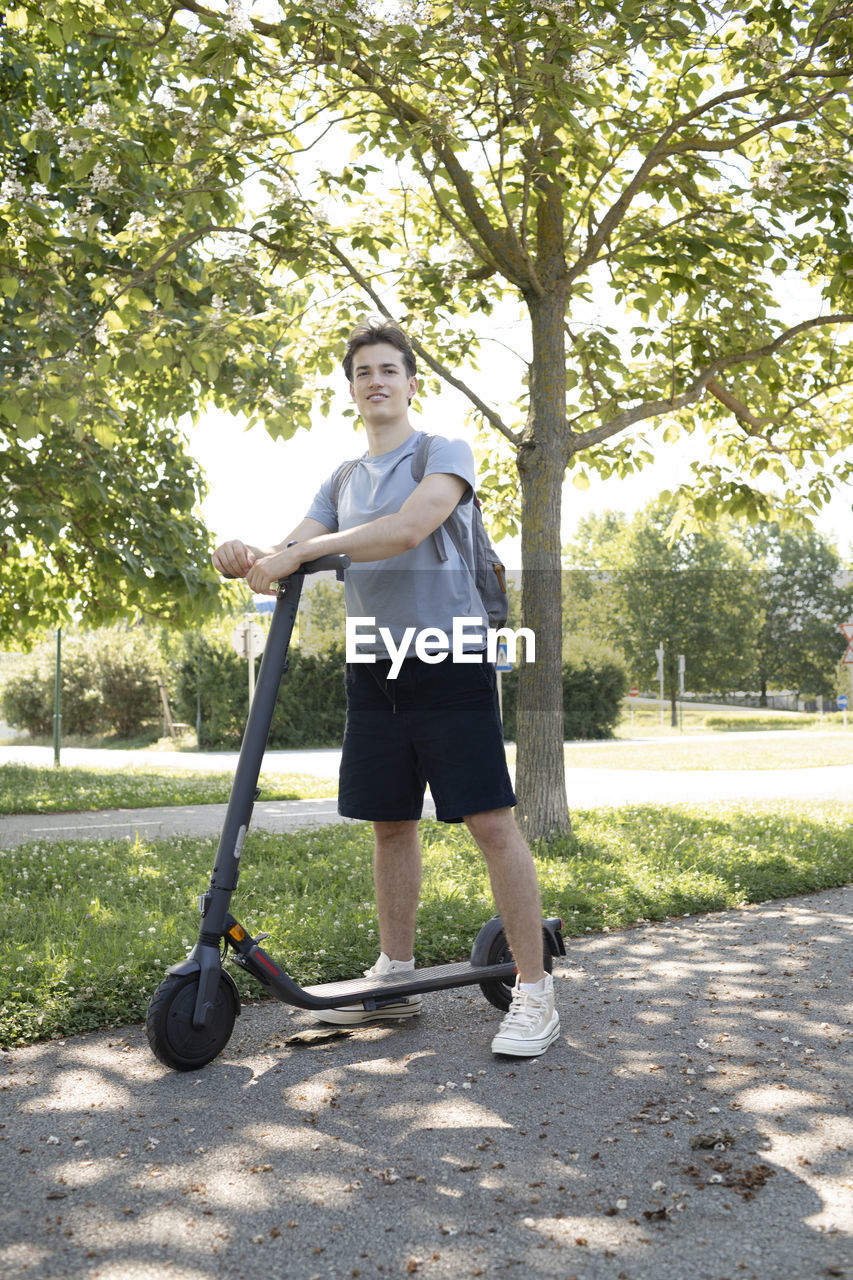 full length, one person, plant, tree, lifestyles, nature, day, adult, sunlight, sports, leisure activity, casual clothing, shadow, lawn, standing, park, front view, young adult, park - man made space, outdoors, men, grass, transportation, exercising, growth, clothing, portrait, looking at camera, women, segway, holding