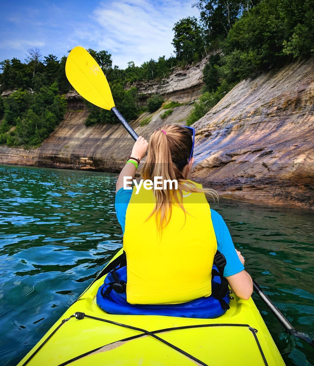 Rear view of woman kayaking in river by mountain in forest