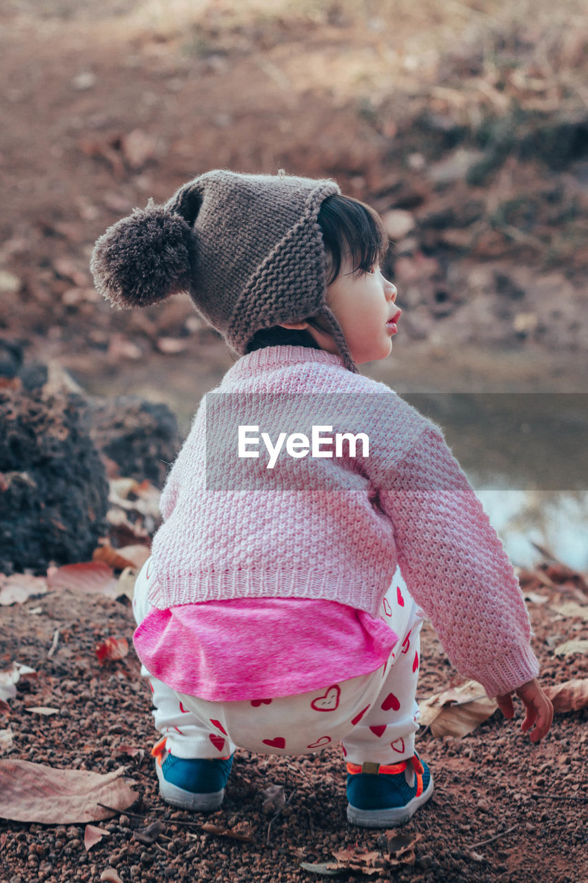 Cute baby girl looking away while crouching on land during winter