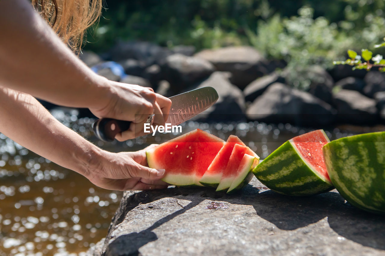 Cropped hand of woman cutting watermelon by lake