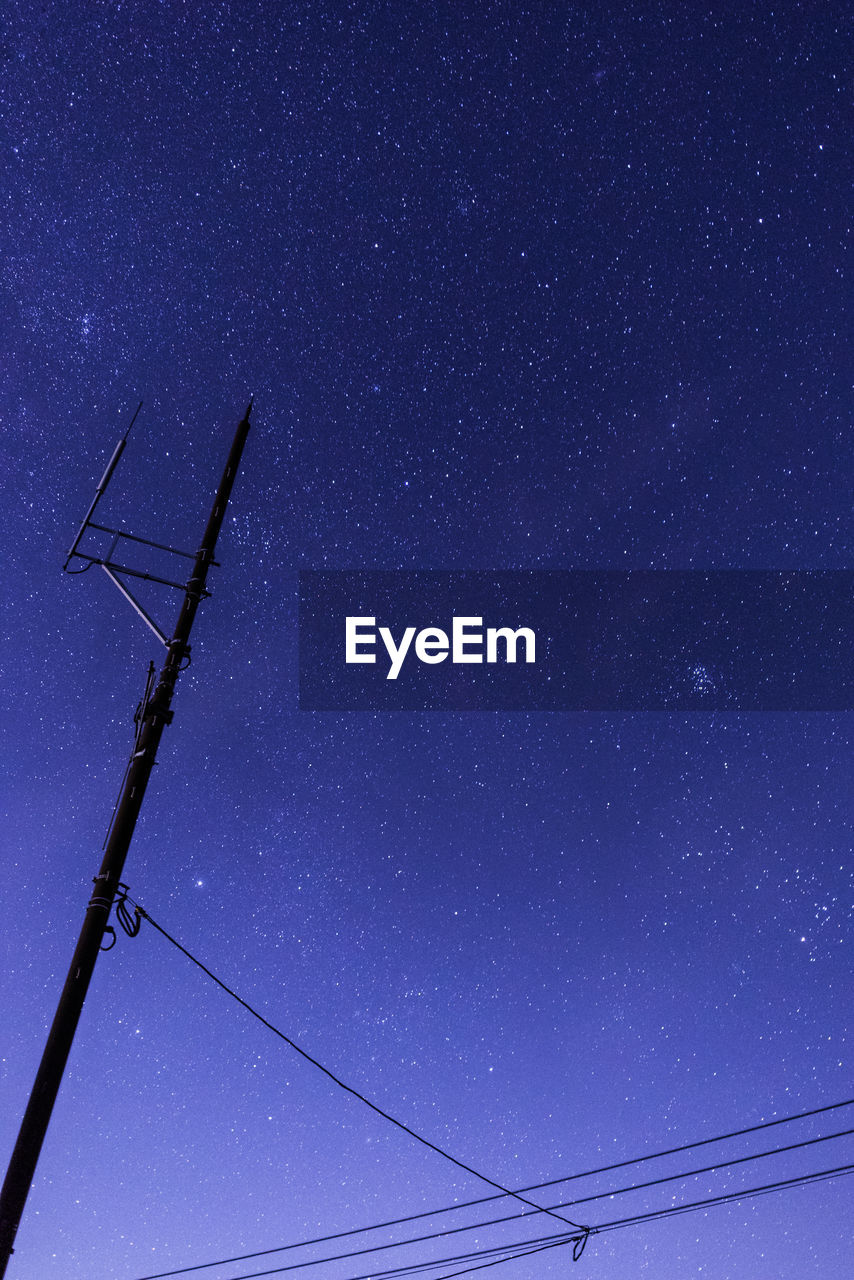 LOW ANGLE VIEW OF ELECTRICITY PYLON AGAINST STAR FIELD AT NIGHT