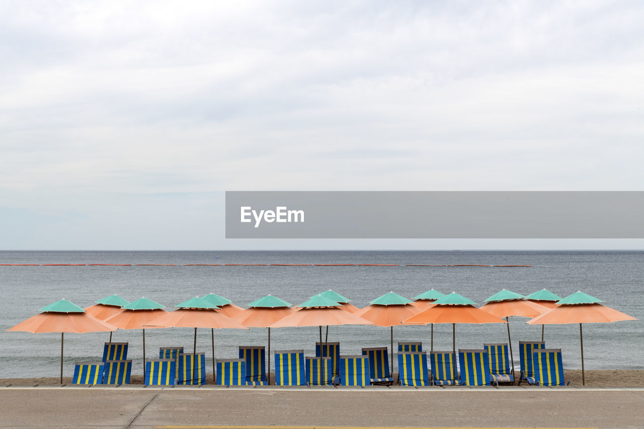 water, sky, sea, horizon over water, beach, horizon, land, cloud, nature, beauty in nature, tranquility, ocean, tranquil scene, scenics - nature, sand, day, body of water, vacation, no people, shore, chair, idyllic, umbrella, coast, in a row, absence, outdoors, parasol, trip, holiday, seat, protection, bay, beach umbrella, travel destinations, blue, relaxation, side by side, architecture, beach hut