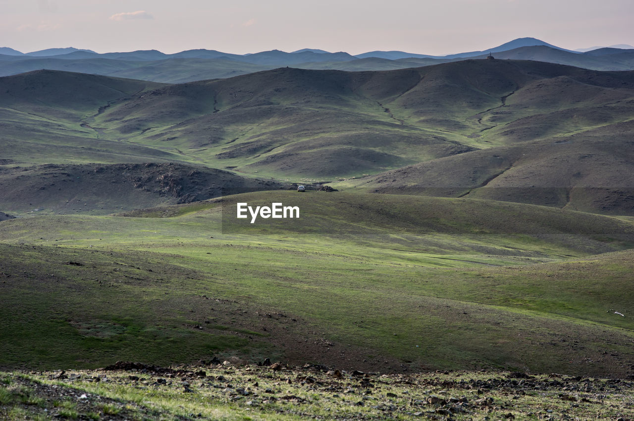A single car parked hillside in mongolias vast landscape amid lush green hills.