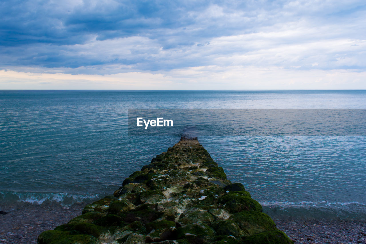 Moss covered groyne at beach against sky