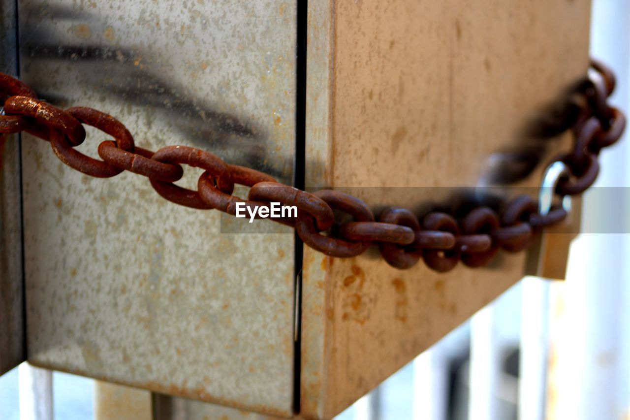 Close-up of metallic box locked with rusty chain