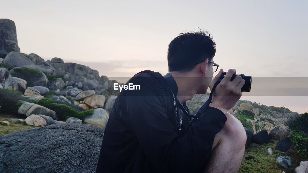 Side view of man photographing on field against sky