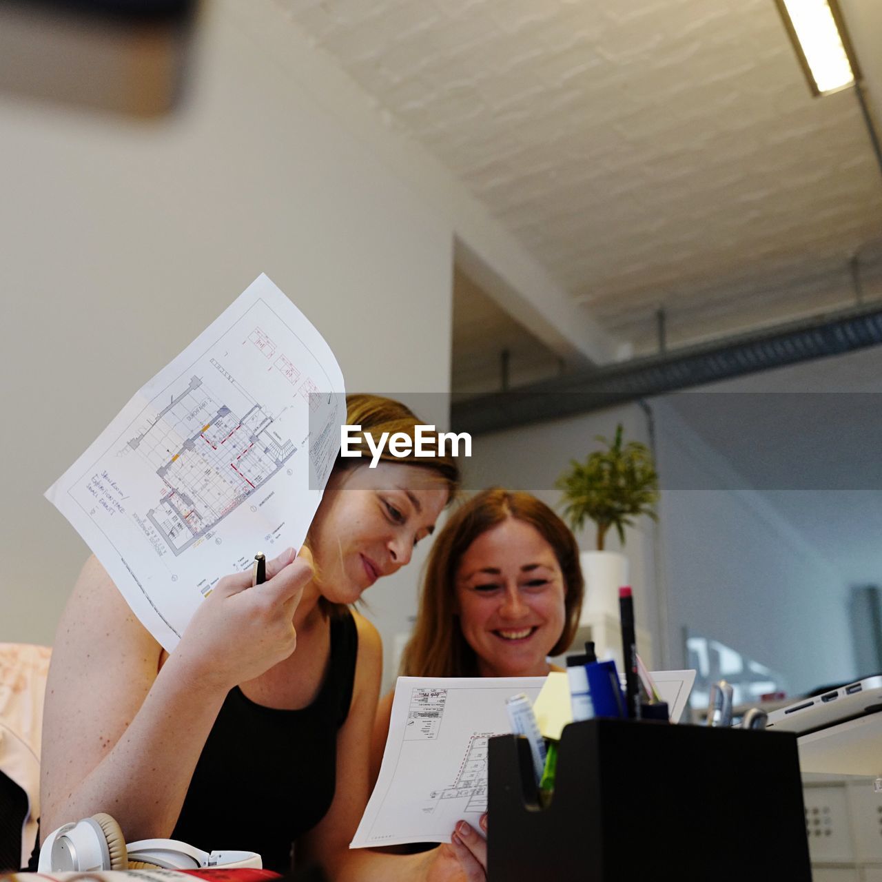 Happy female colleagues discussing blueprints in office