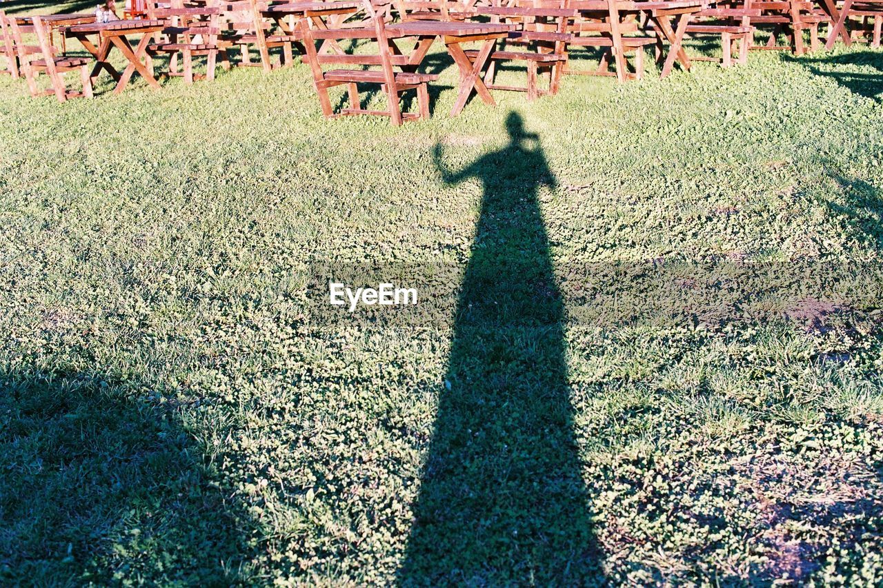 Shadow of man on grass by picnic tables