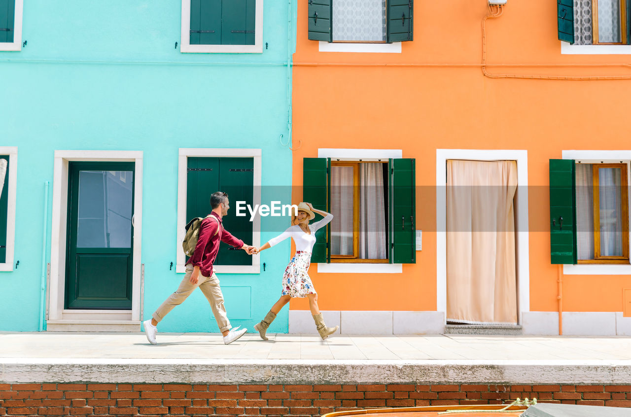 Couple holding hands while walking on sidewalk by building in city