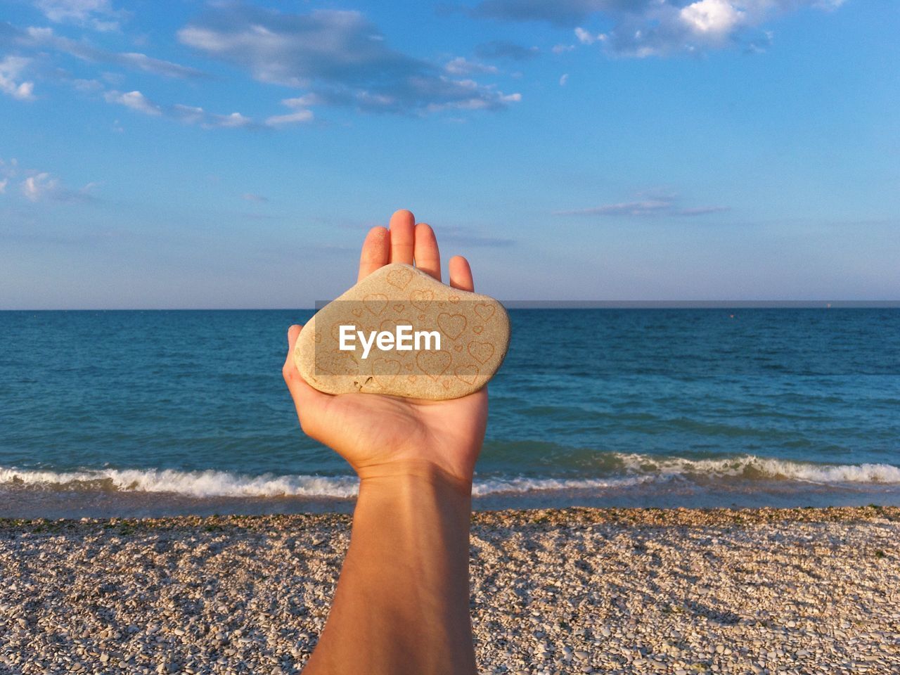 Cropped image of woman holding stone against sea