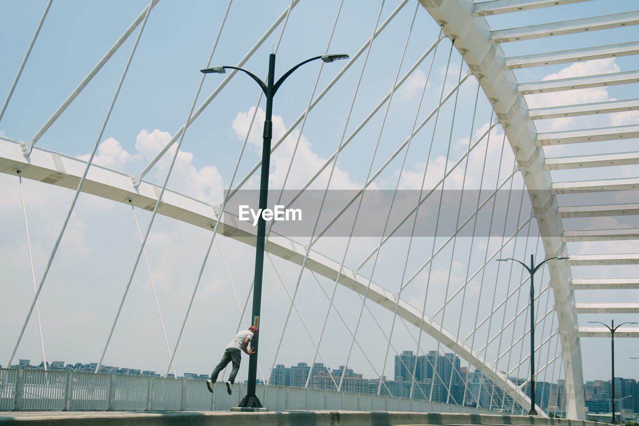 Man levitating on arch bridge against cloudy sky