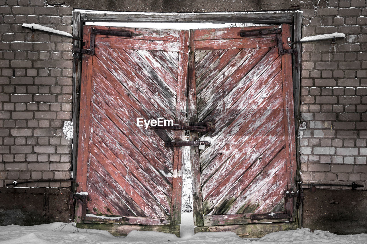 Broken locked door amidst brick wall during winter