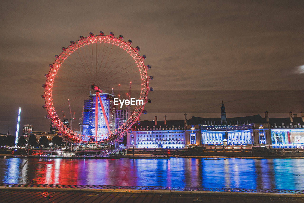 ILLUMINATED FERRIS WHEEL BY RIVER AGAINST SKY