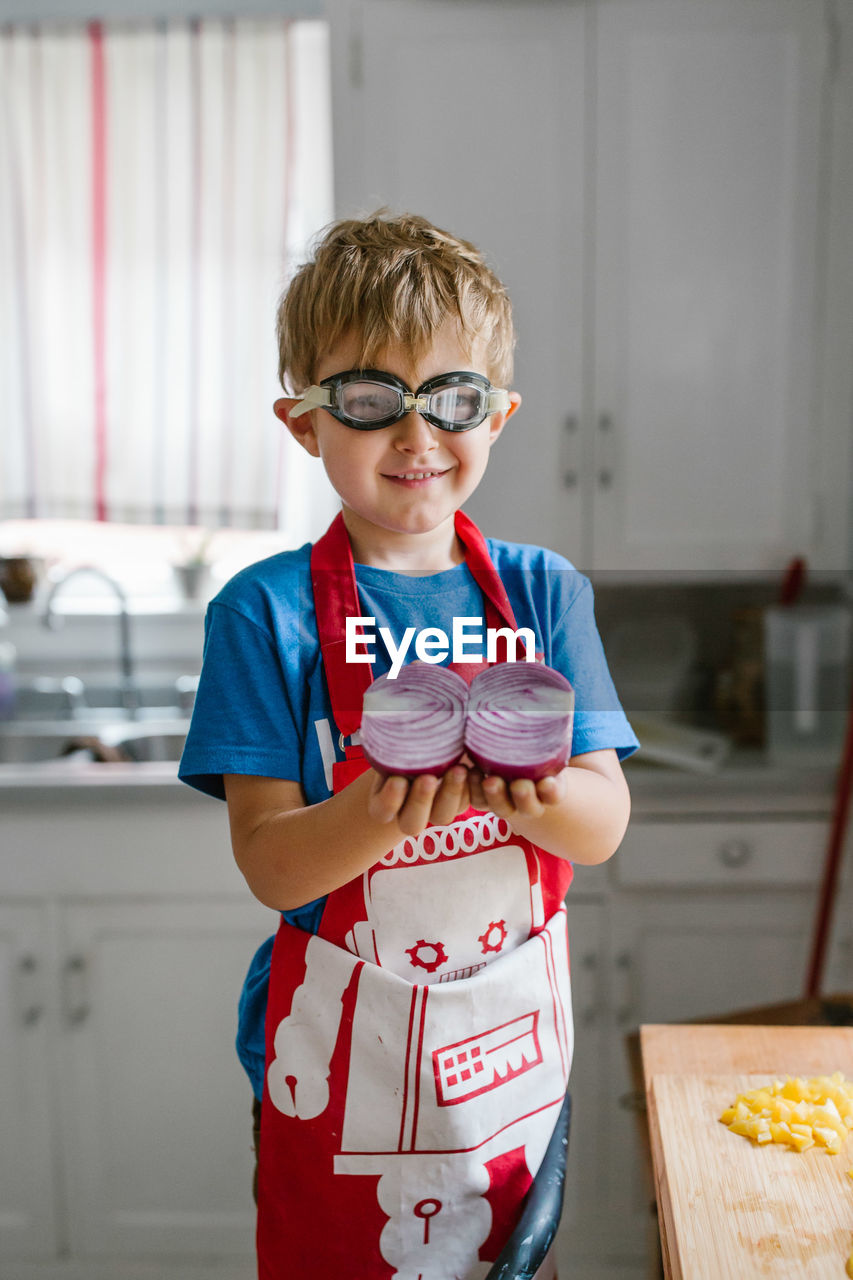 Boy holding halved onion in kitchen at home