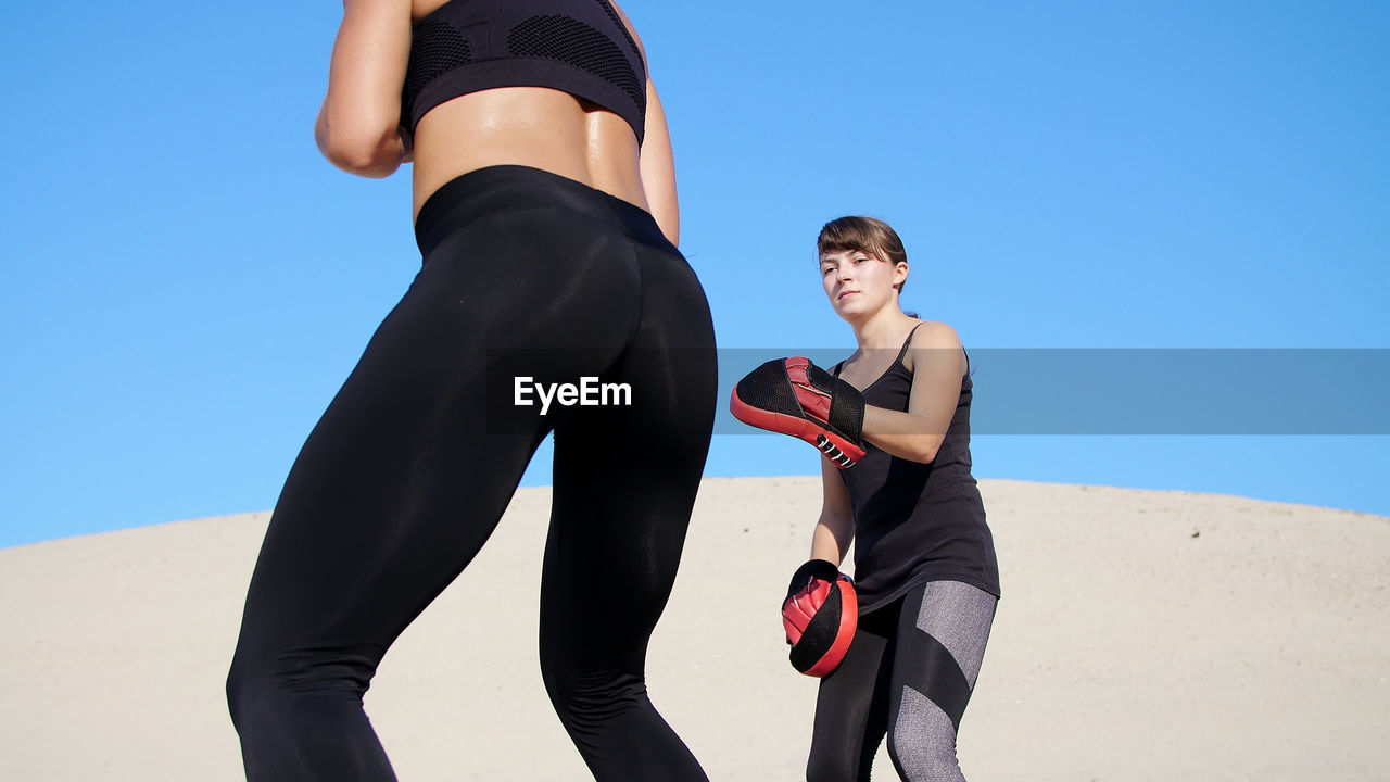 Two athletic, young women in black fitness suits are engaged in a pair work out kicks train to fight