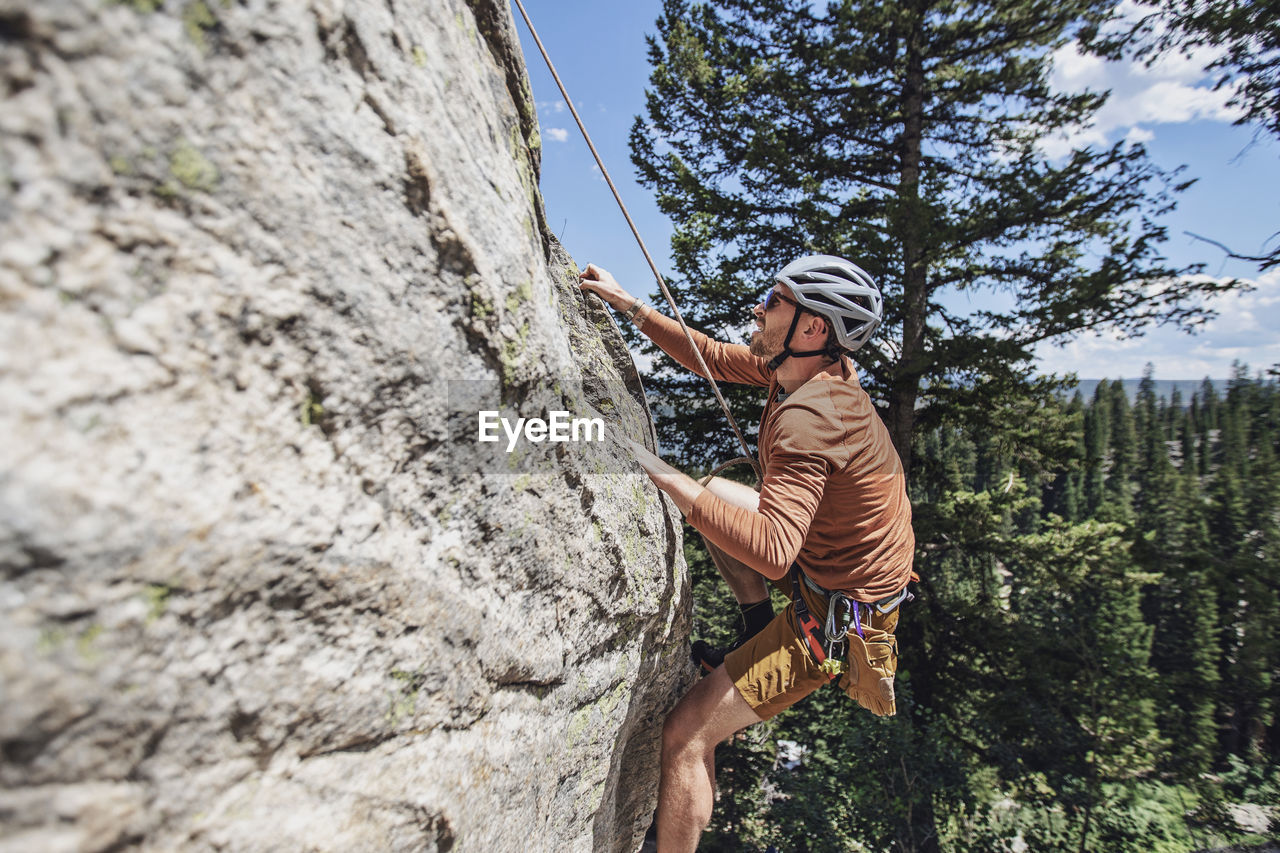 Man holds on to rock with fingertips while climbing with a rope