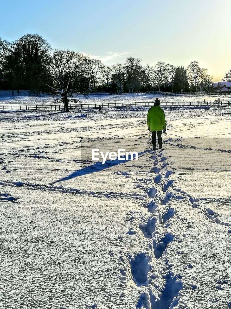 Rear view of man walking on snowy field against sky