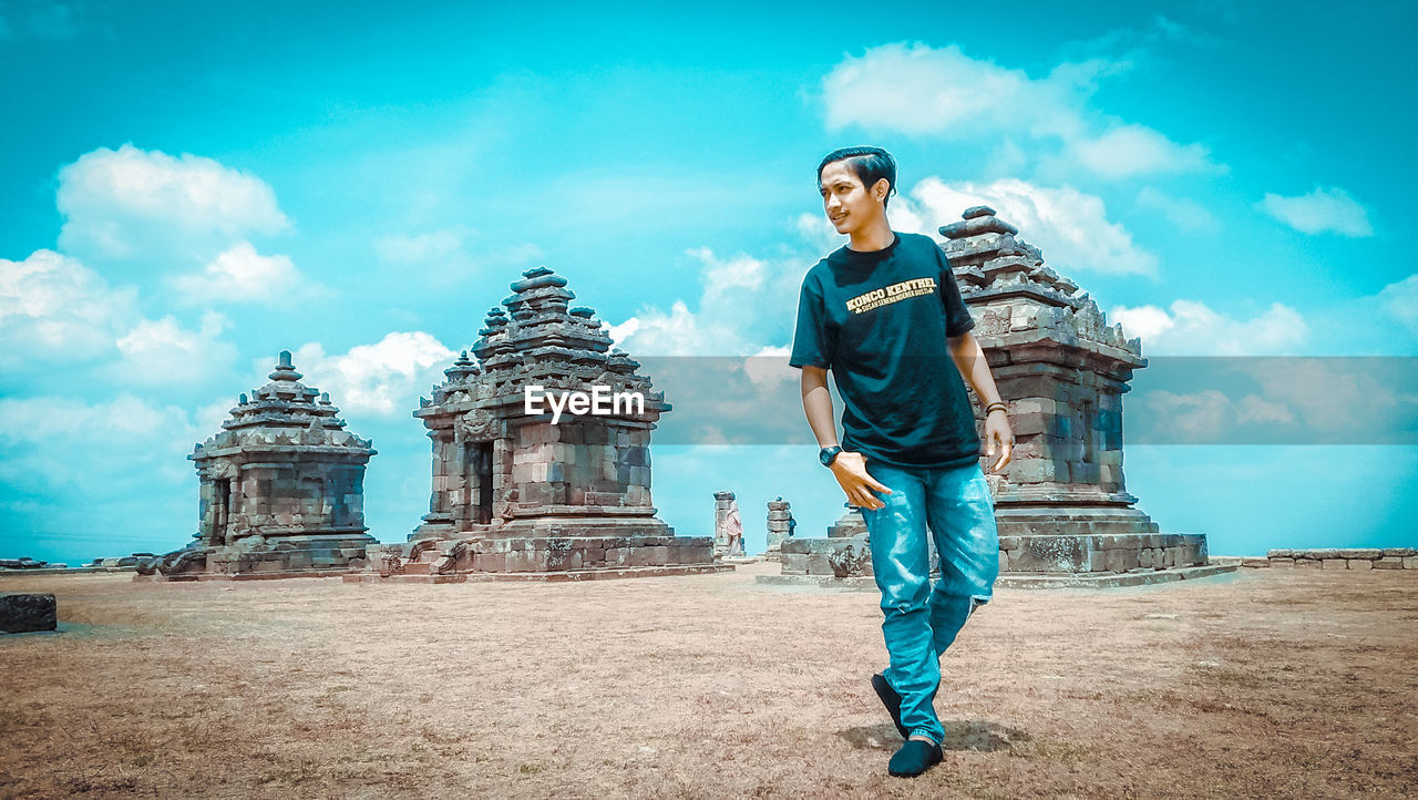 FULL LENGTH OF YOUNG MAN STANDING AGAINST CLOUDY SKY