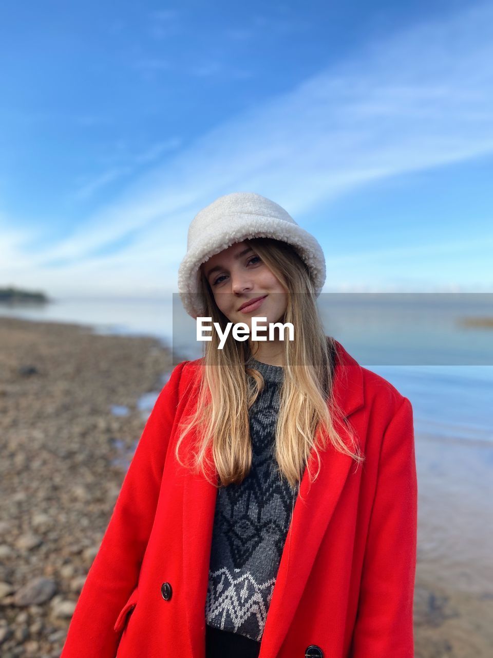 portrait of young woman standing at beach against sky