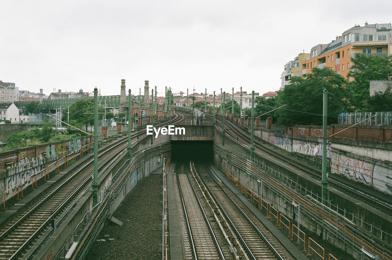 HIGH ANGLE VIEW OF RAILROAD TRACKS AMIDST BUILDINGS AGAINST SKY