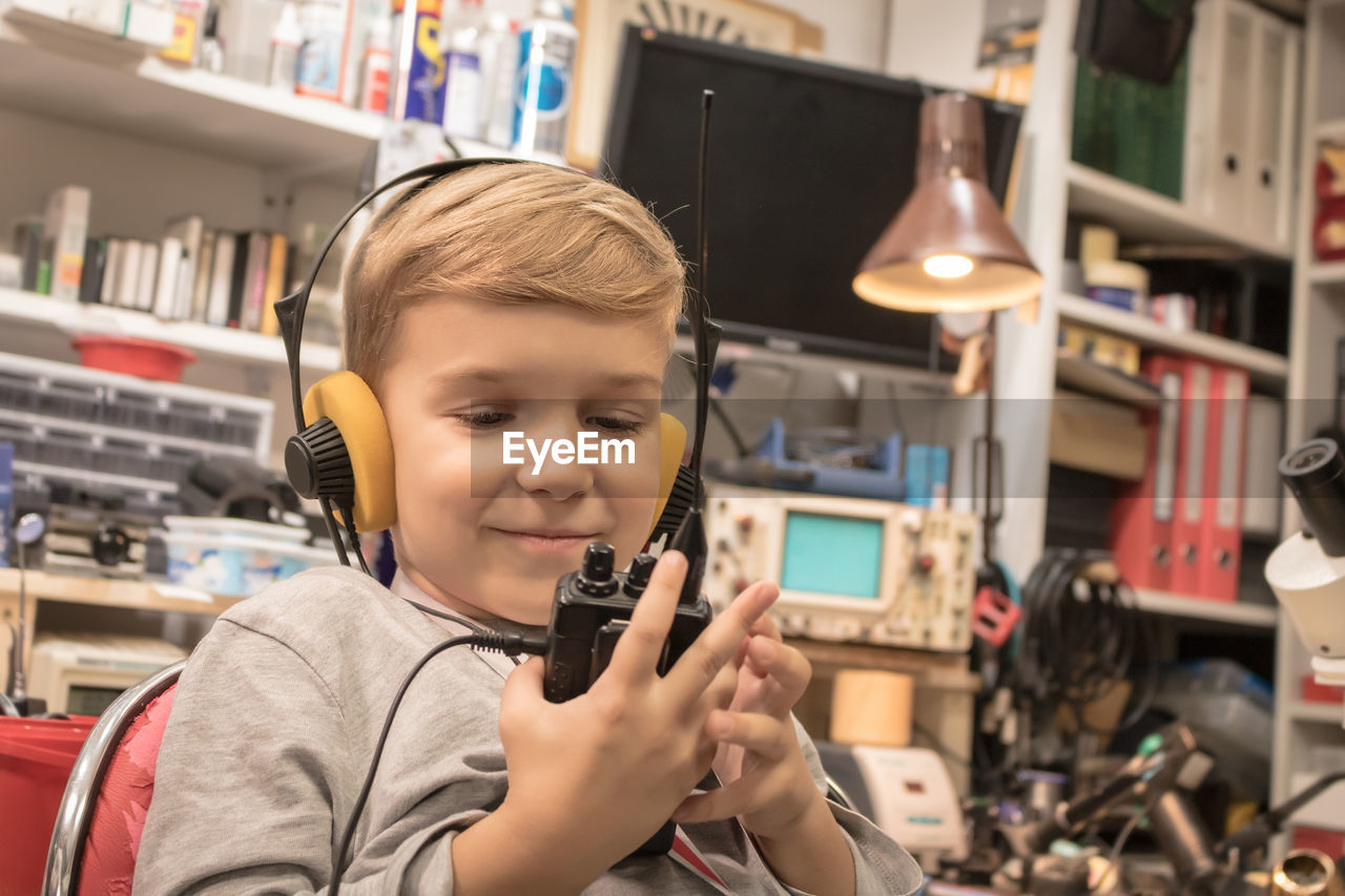 Smiling boy holding walkie-talkie while sitting in workshop