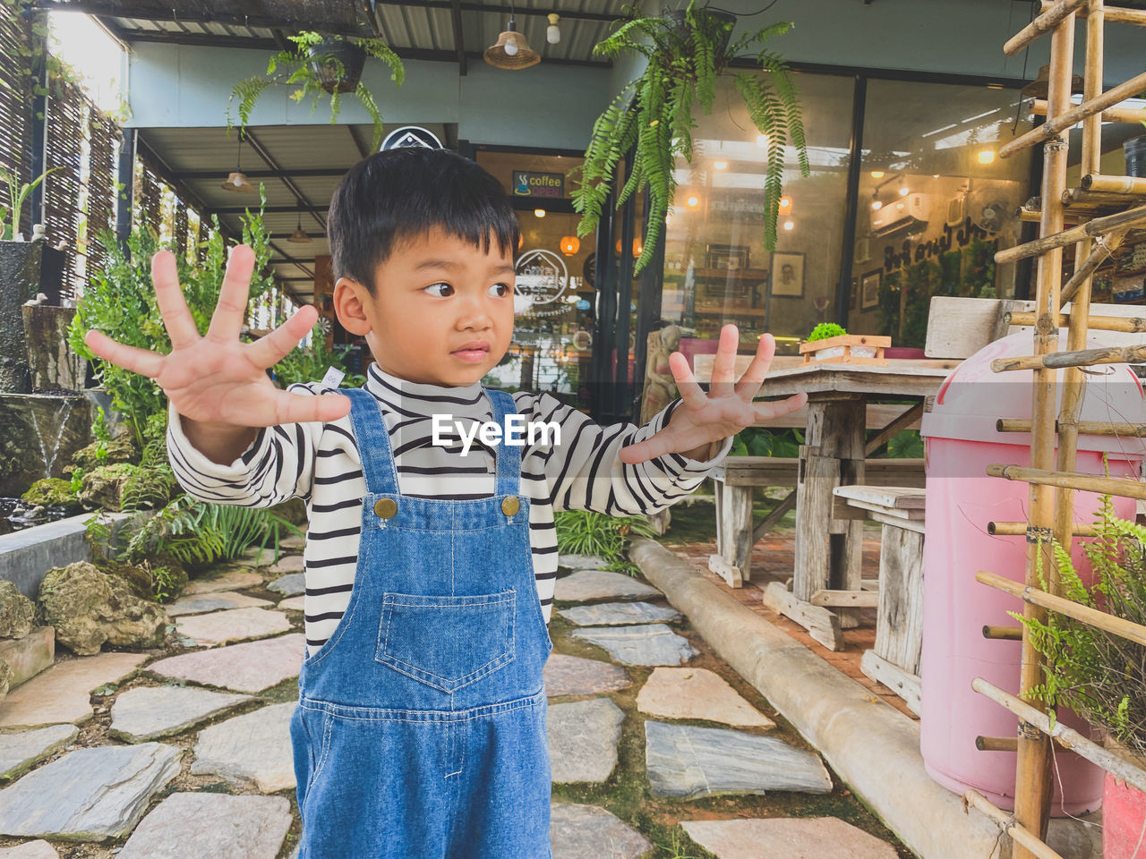 childhood, one person, child, men, standing, cute, vacation, casual clothing, portrait, innocence, lifestyles, looking at camera, smiling, plant, arm, happiness, toddler, clothing, front view, female, nature, emotion, leisure activity, outdoors, flower, gesturing, spring, person, black hair, hand, architecture