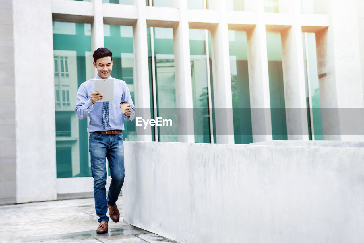 Businessman using digital tablet while walking against building