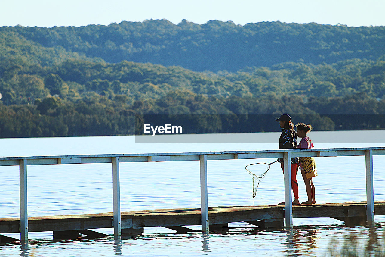 PEOPLE STANDING BY RAILING ON LAKE