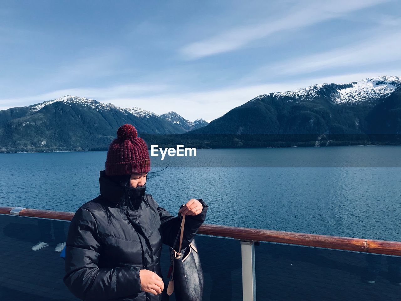 Woman standing by railing over lake against mountains and sky