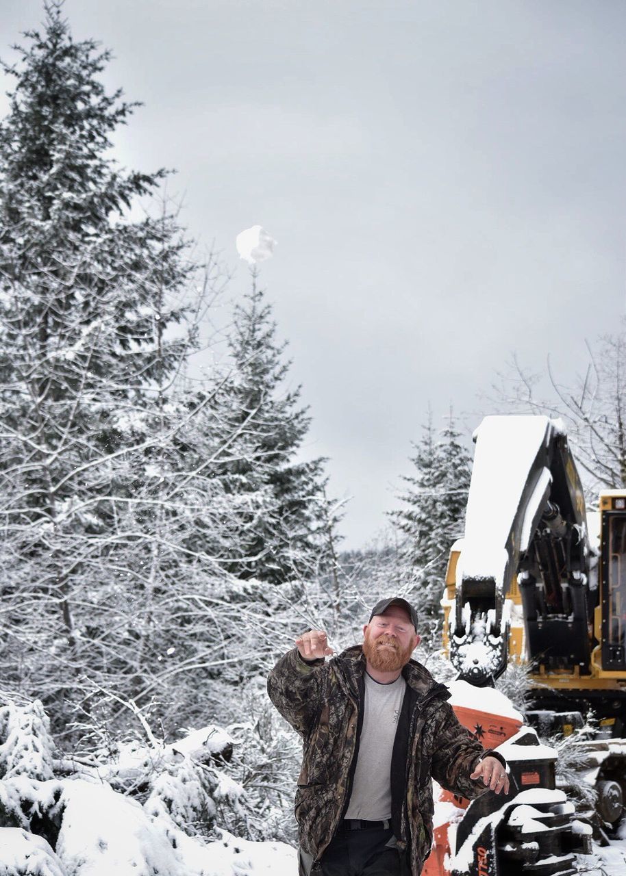 MAN STANDING ON SNOW COVERED TREE