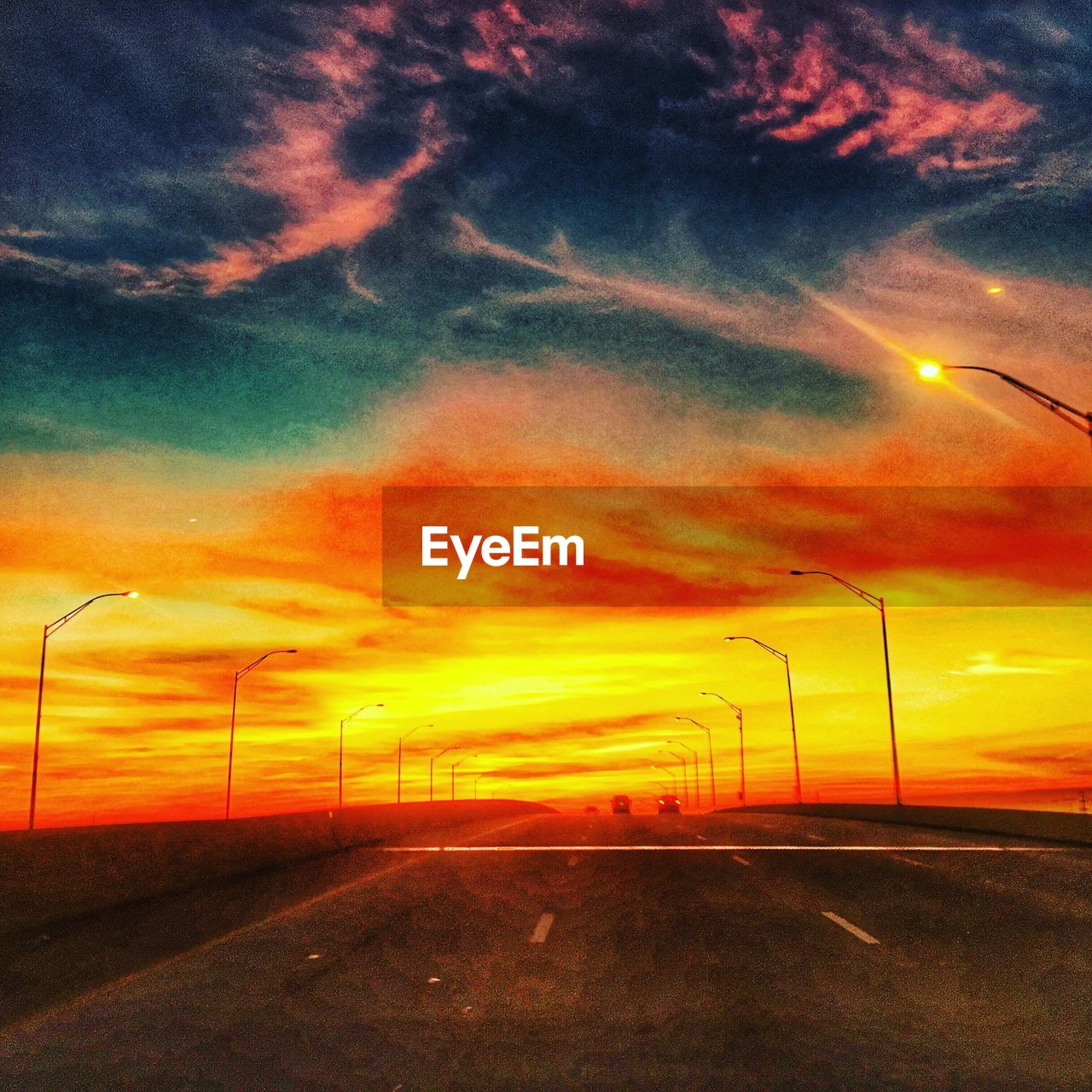 VIEW OF COUNTRY ROAD AGAINST ORANGE SKY