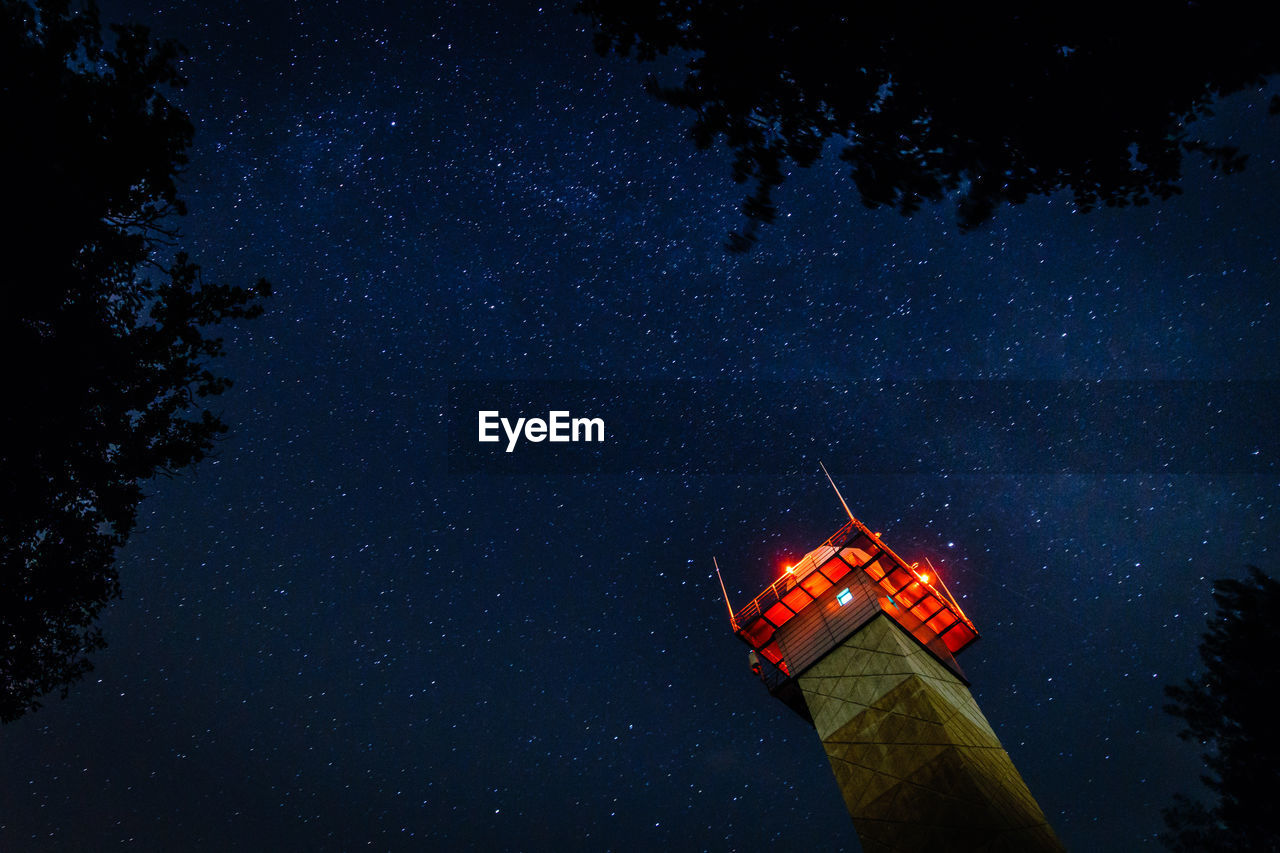 Low angle view of illuminated tower against star field