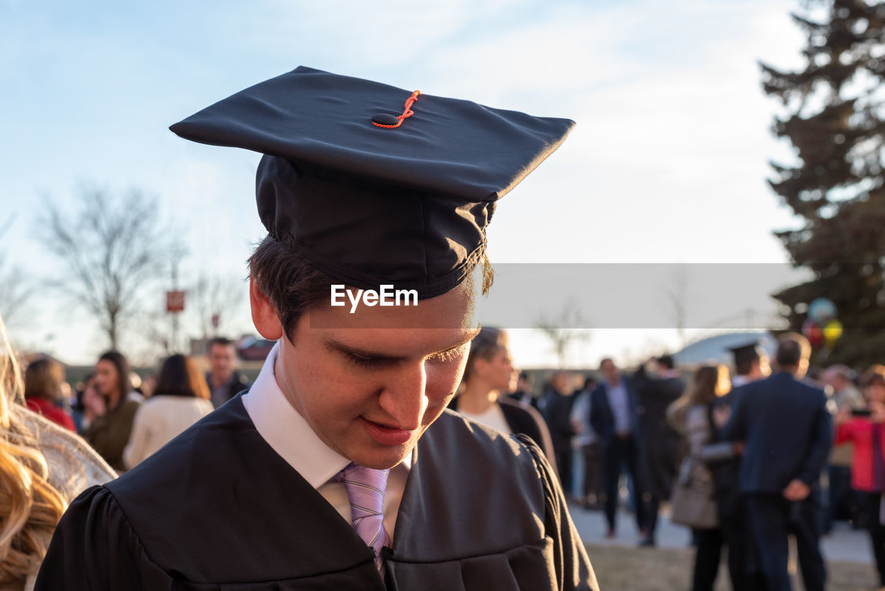 Close-up of young man wearing graduation gown against sky