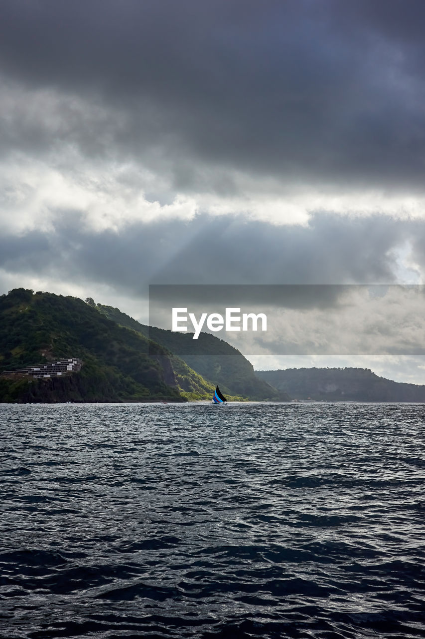 A lone sailboat and an island under threatening skies