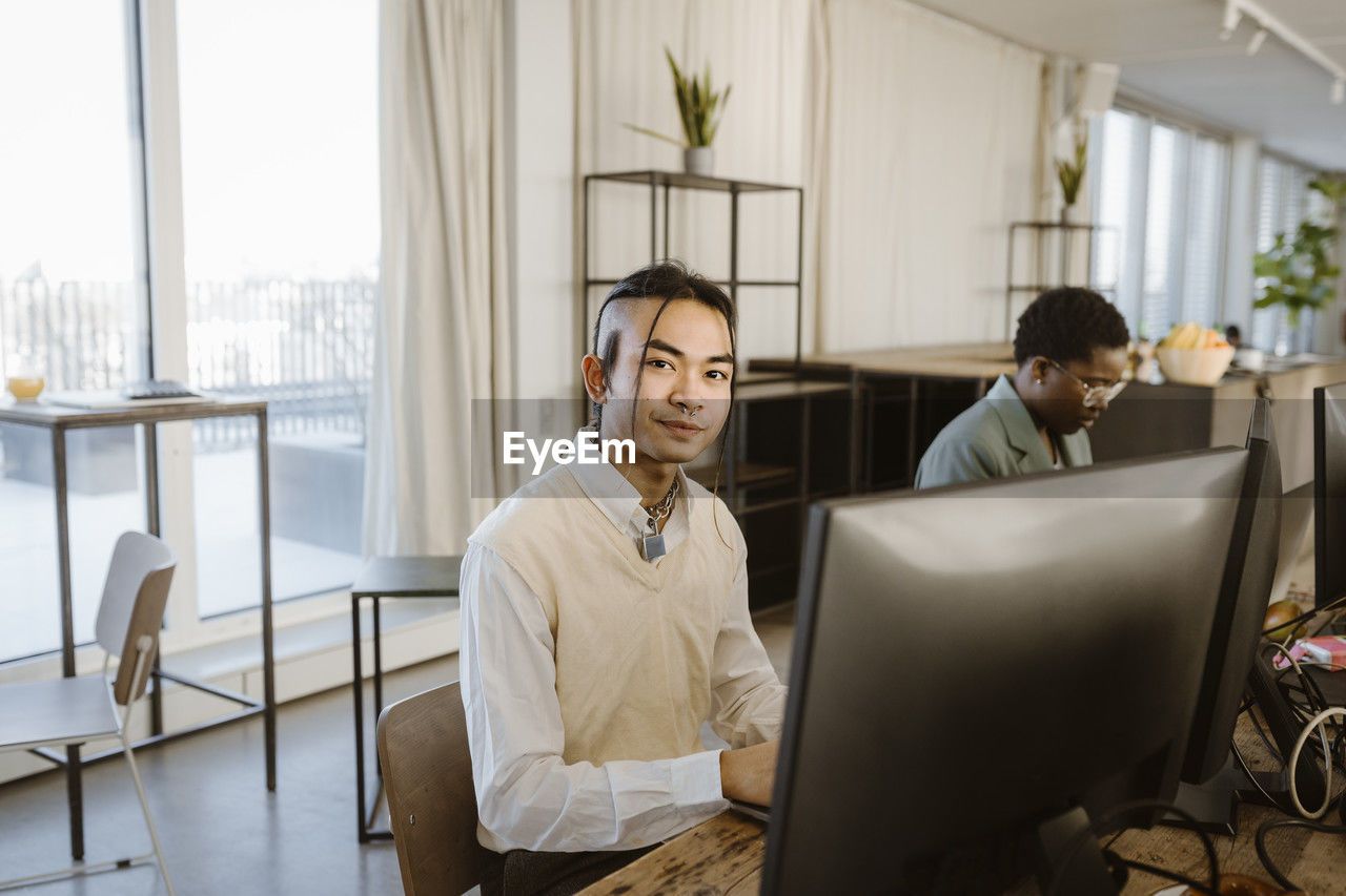 Portrait of hipster young male programmer sitting at computer desk in office