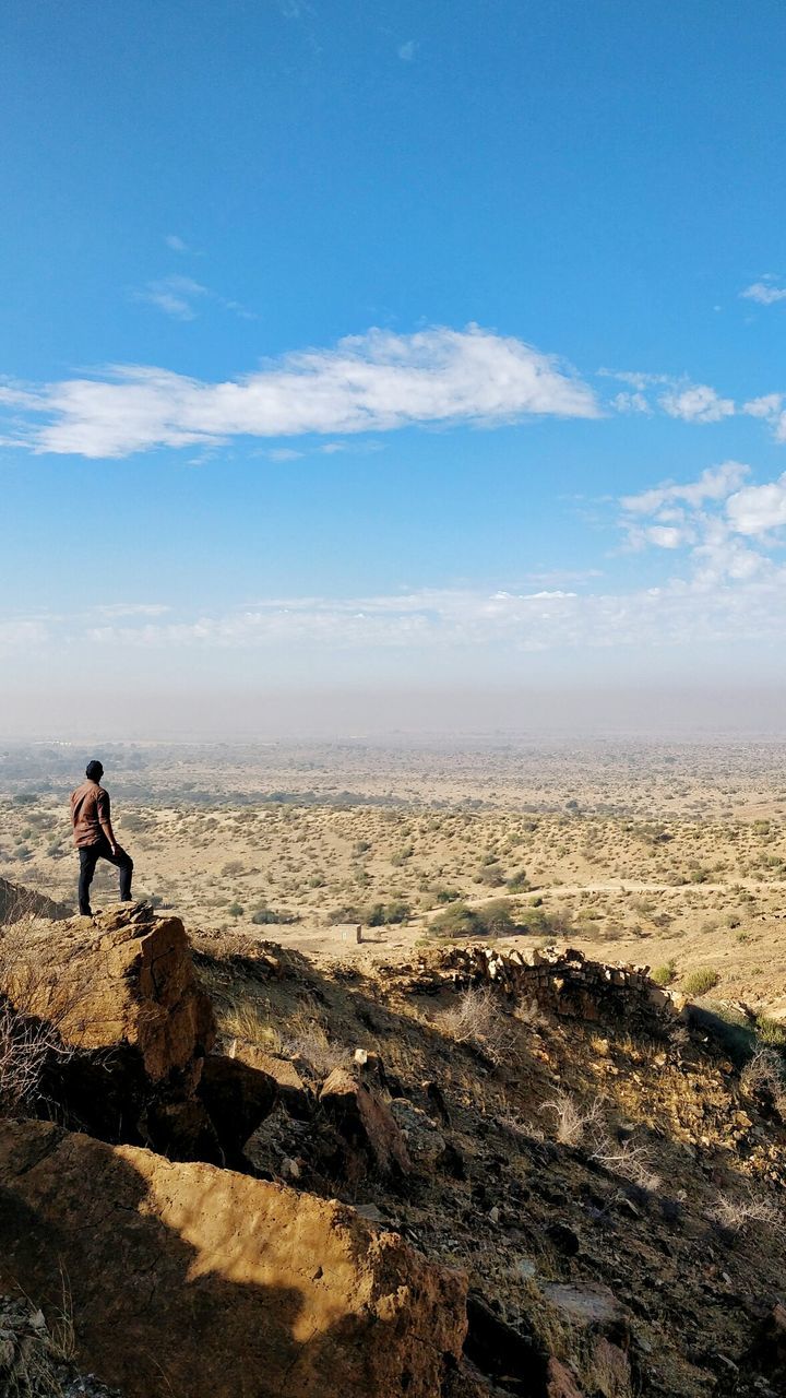 Rear view of man standing on cliff against blue sky