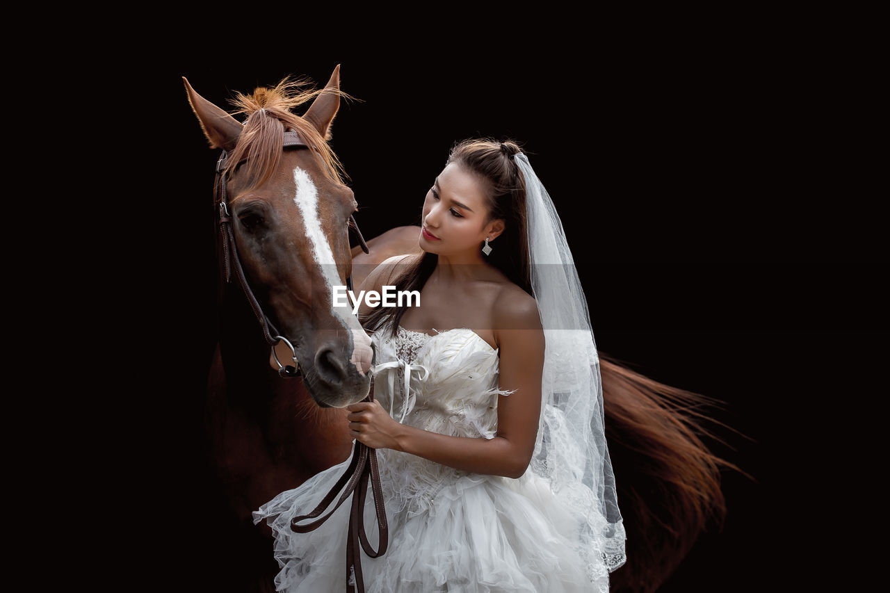 Woman in wedding dress with horse against black background