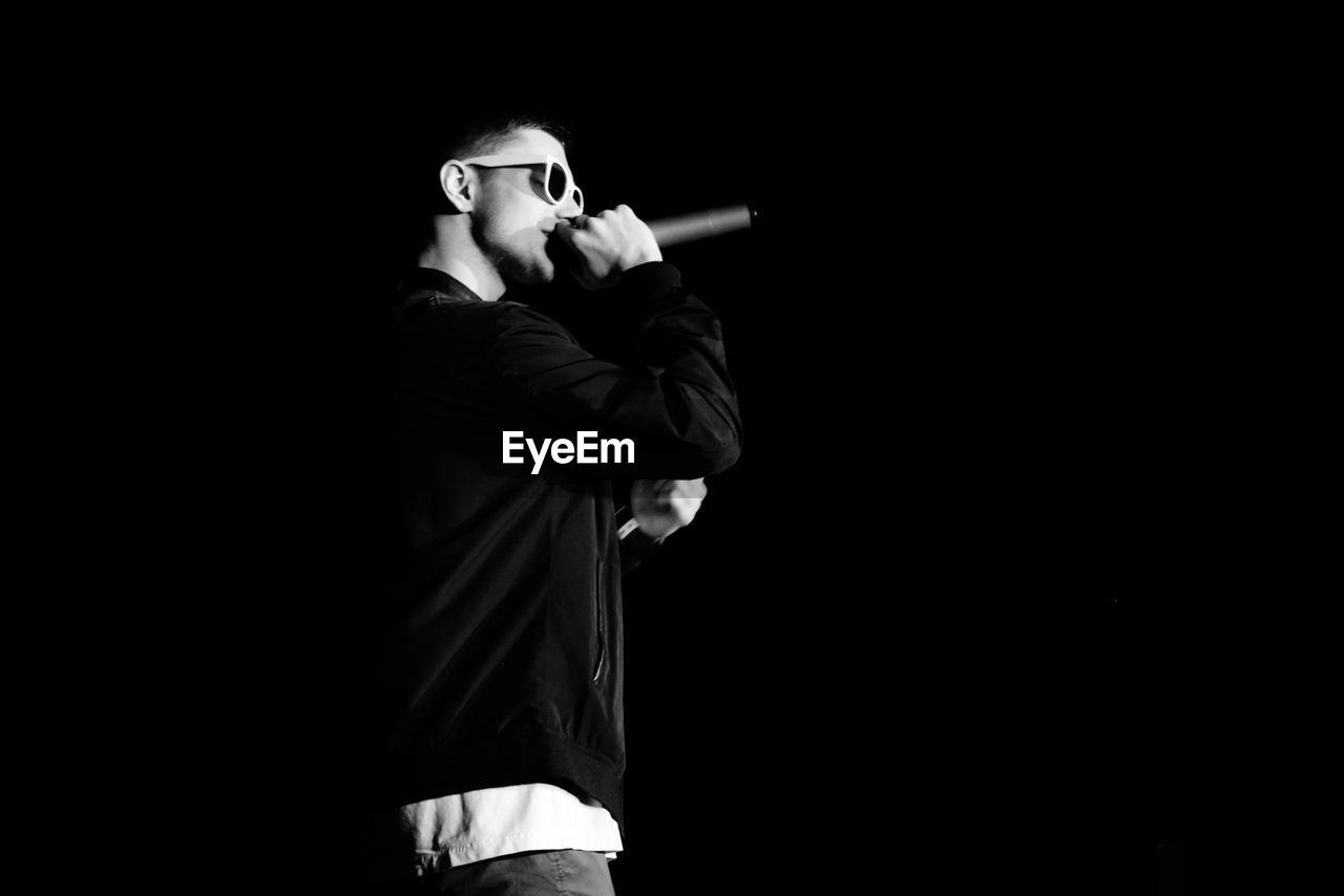 Side view of young man singing against black background