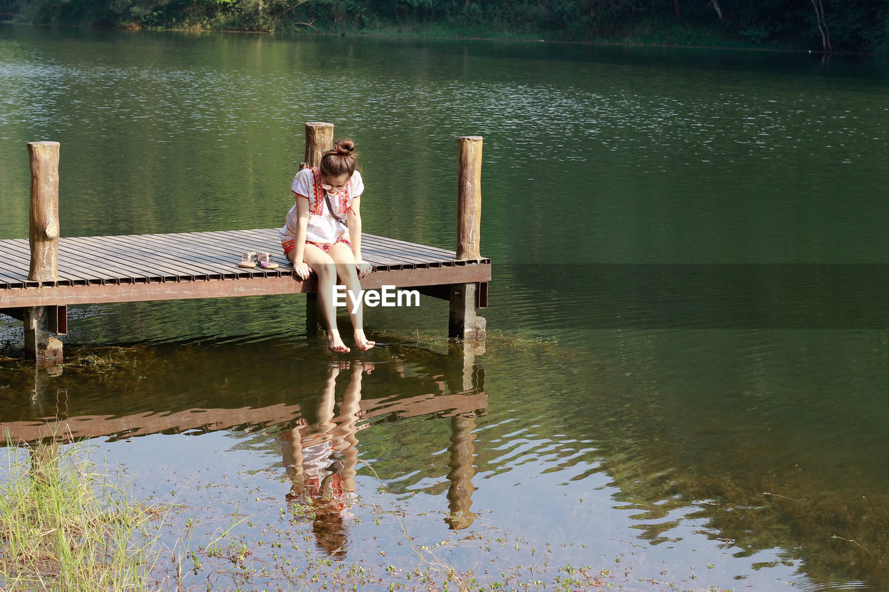 Woman sitting on pier over lake