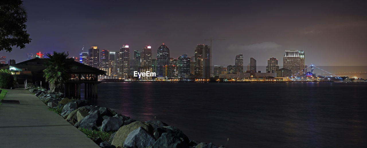 Illuminated buildings by river against sky at night