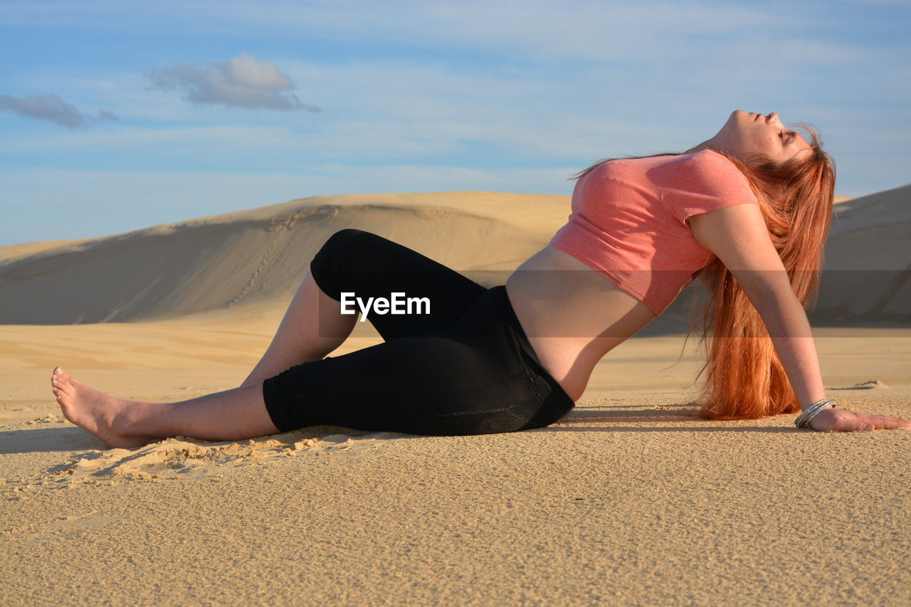 Full length young woman lying on sand at desert