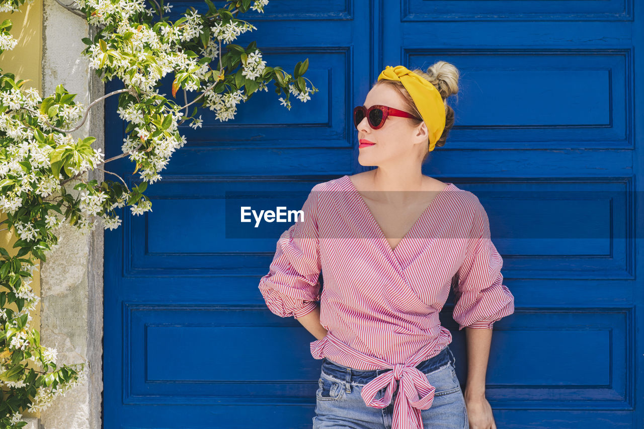 Woman in sunglasses looking away while standing against door