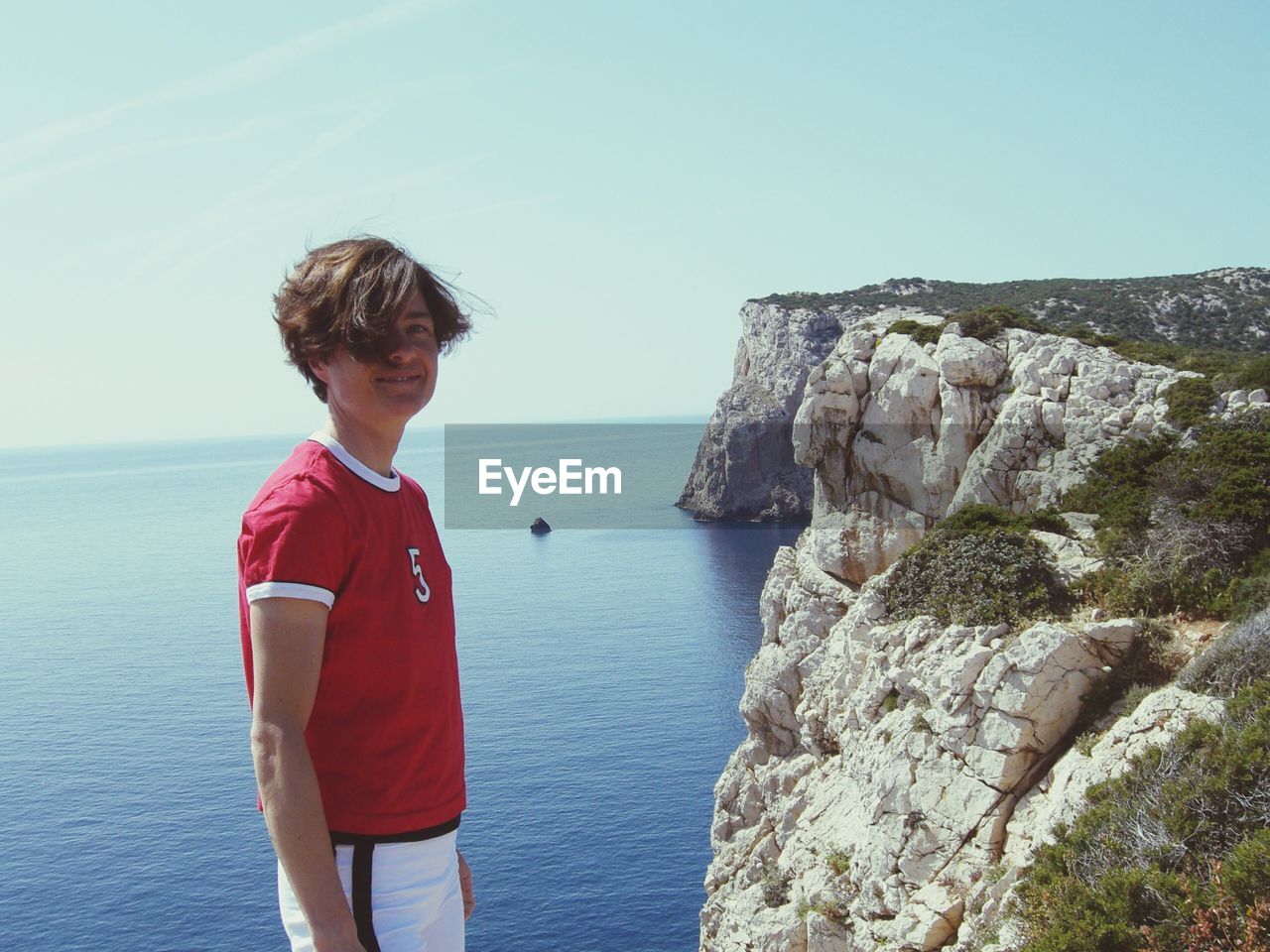 Portrait of smiling mature woman standing against rock formations by sea