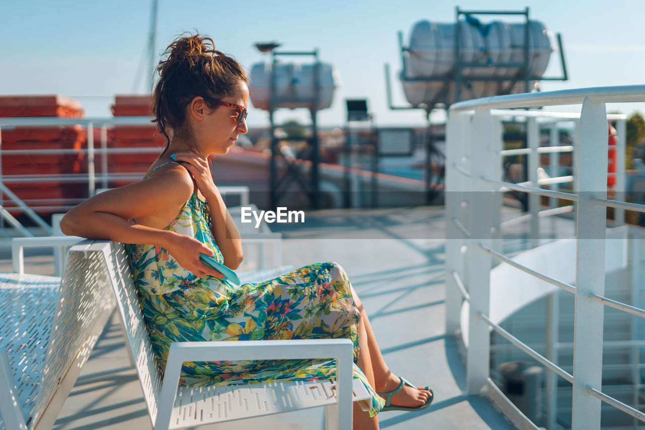 Side view of young woman sitting by railing on bench