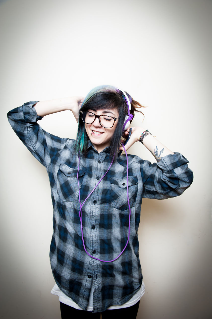 Young woman listening music through headphones against white background