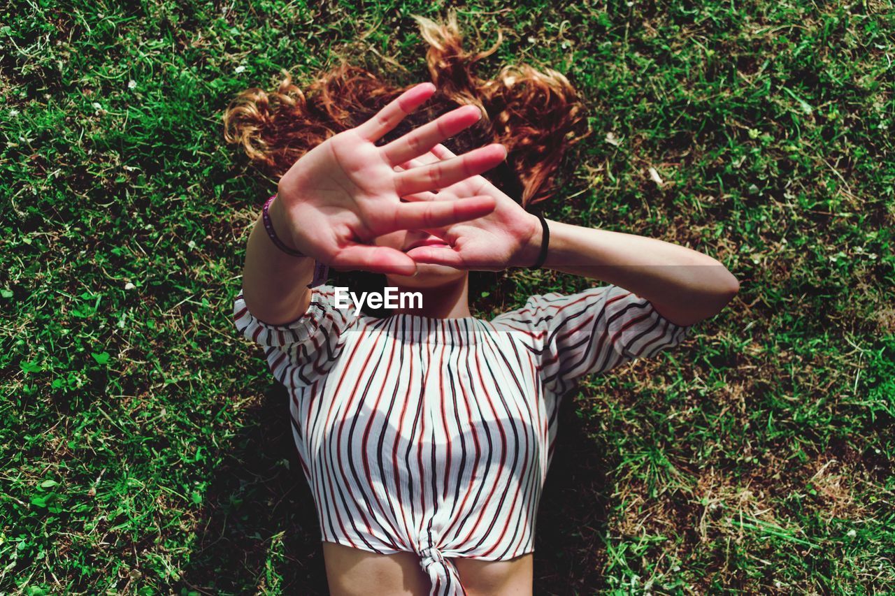 High angle view of woman covering face with hands while lying on field