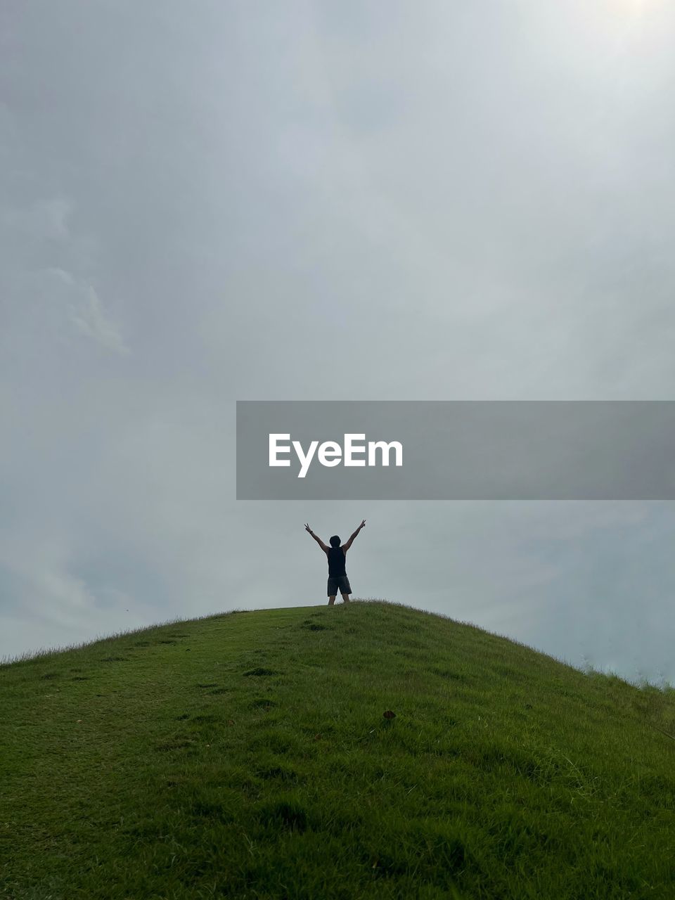 hill, sky, wind, grass, cloud, nature, arm, environment, one person, grassland, beauty in nature, arms raised, limb, land, plant, landscape, horizon, tranquility, non-urban scene, day, field, scenics - nature, green, leisure activity, sea, standing, tranquil scene, meadow, outdoors, human limb, idyllic, plain, rural area, arms outstretched, full length, lifestyles, rear view, remote, sunlight, prairie, adult