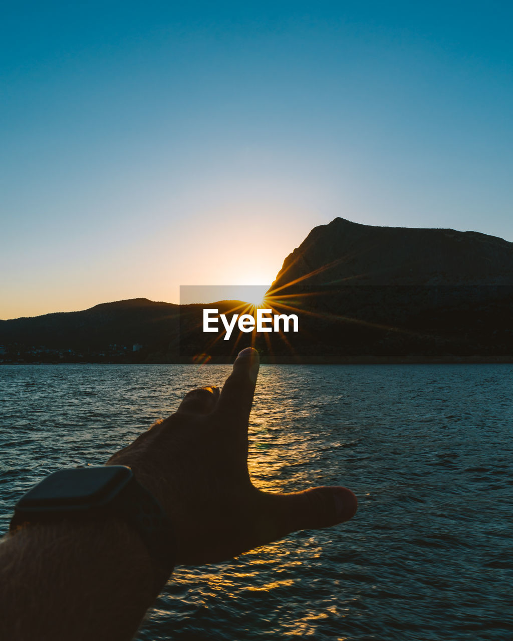 Cropped hand against sea during sunset