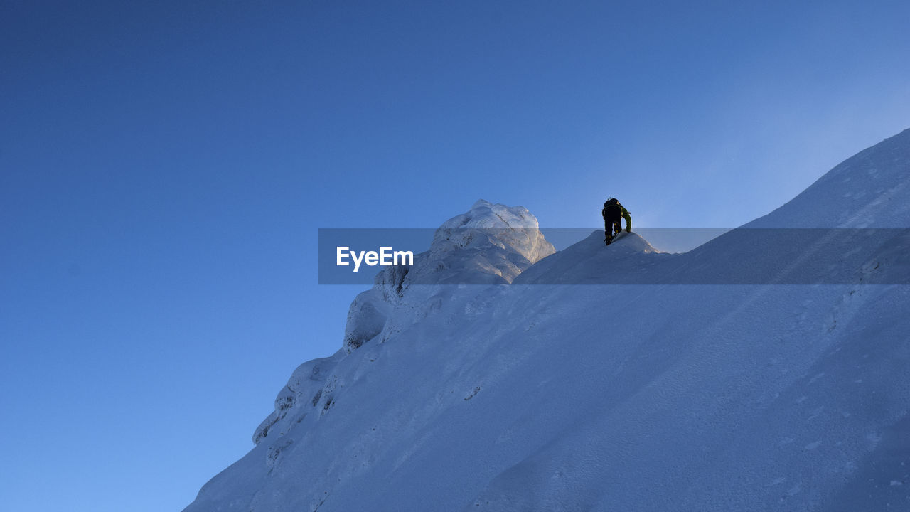 MAN SKIING ON SNOWCAPPED MOUNTAIN AGAINST CLEAR BLUE SKY